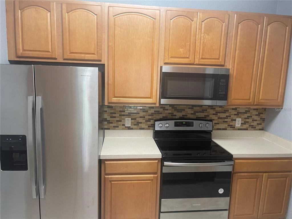 A kitchen features light wood cabinets, stainless steel appliances, and a mosaic tile backsplash — 6451 OLD PARK LN UNIT 102, ORLANDO, FL