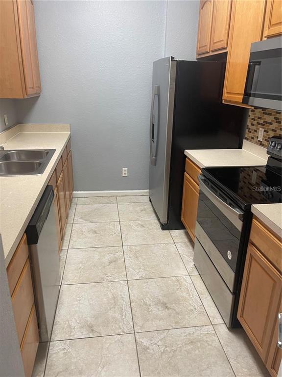 A kitchen features light-colored countertops, wood cabinets, stainless steel appliances, and tiled flooring — 6451 OLD PARK LN UNIT 102, ORLANDO, FL