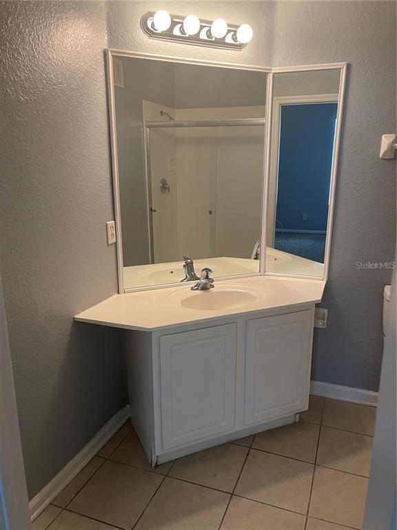A bathroom vanity with a white cabinet, countertop, and a multi-paneled mirror — 6451 OLD PARK LN UNIT 102, ORLANDO, FL