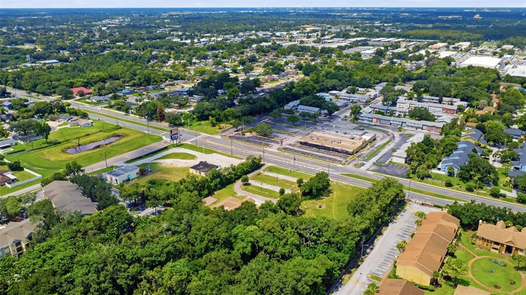 An aerial view shows a commercial plaza, surrounding residential buildings, and dense trees near roads — 3075 N GOLDENROD ROAD, WINTER PARK, FL