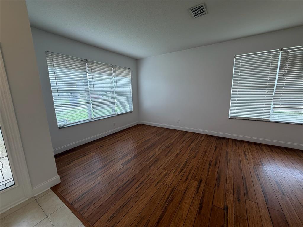 An empty room features dark wood flooring, white walls, and windows with horizontal blinds — 2445 CYPRESS TRACE CIRCLE, ORLANDO, FL
