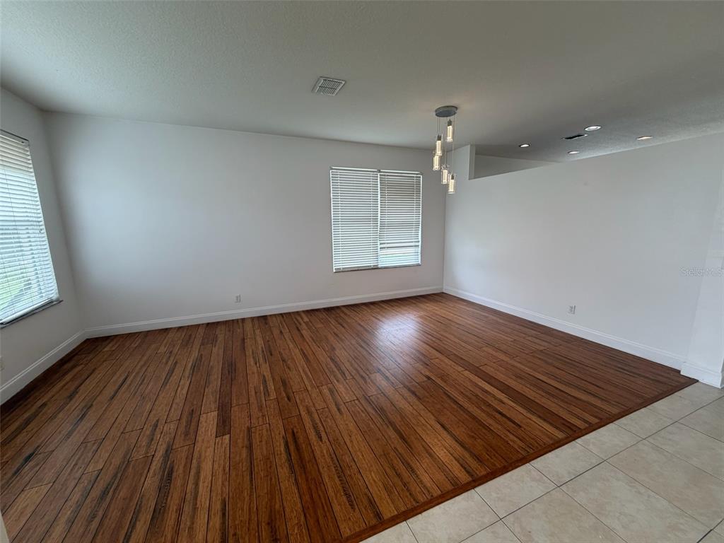 An empty room features dark wood flooring, white walls, and a modern pendant light fixture — 2445 CYPRESS TRACE CIRCLE, ORLANDO, FL