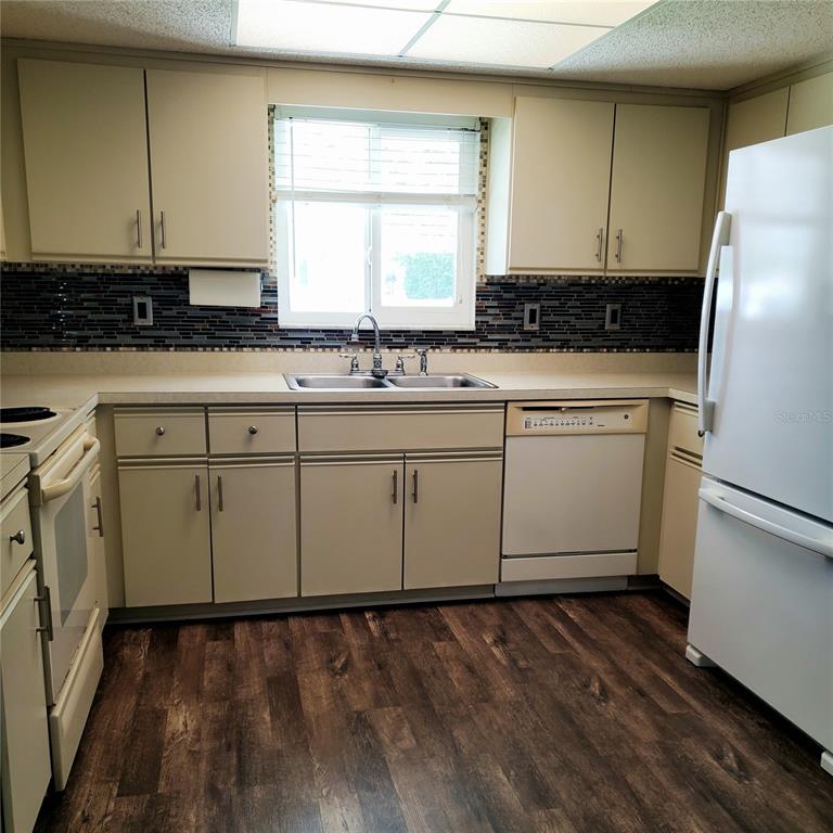 A kitchen features beige cabinets, a dark tile backsplash, white appliances, and wood-look flooring — 6311 SW 106TH PLACE, OCALA, FL