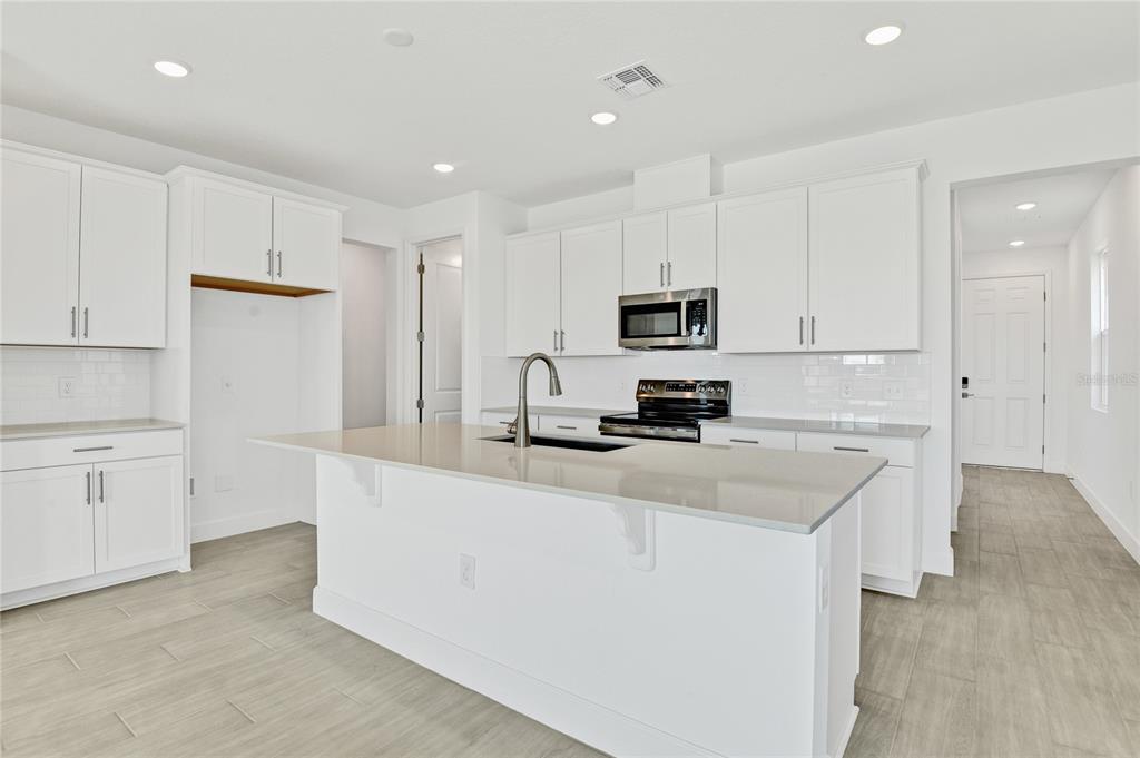 A modern kitchen features white cabinetry, a large center island, and light-colored tile flooring — 1693 CROOKED CREEK STREET, ST CLOUD, FL