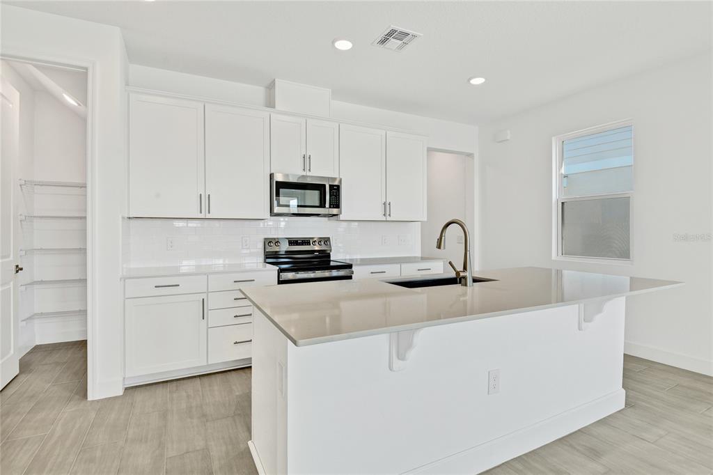 A modern kitchen features white cabinets, stainless steel appliances, a quartz island, and tile flooring — 1693 CROOKED CREEK STREET, ST CLOUD, FL