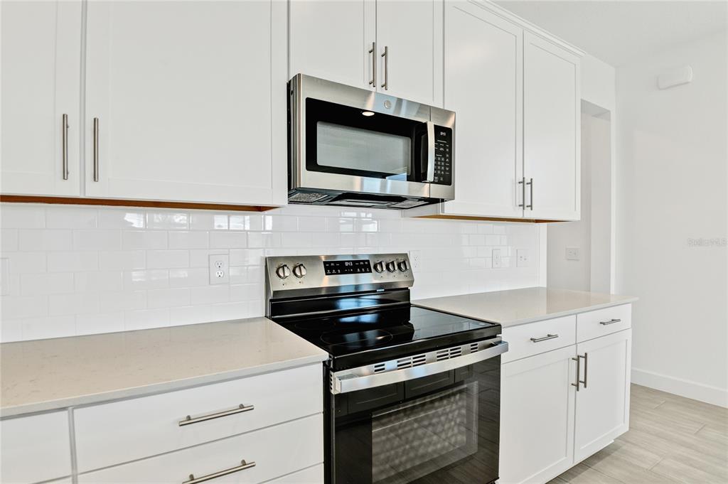 A kitchen features white cabinets, stainless steel appliances, and a white subway tile backsplash — 1693 CROOKED CREEK STREET, ST CLOUD, FL