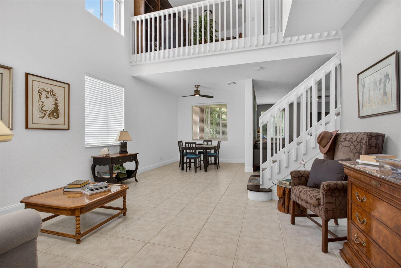 A bright living and dining area features tile floors, a staircase, and a loft balcony — 5133 Heron Place, Coconut Creek FL 33073, COCONUT CREEK, FL