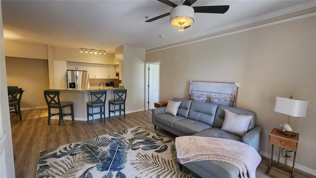 An open-concept living room and kitchen featuring a gray sectional sofa and breakfast bar seating — 4106 CENTRAL SARASOTA PARKWAY UNIT 1026, SARASOTA, FL