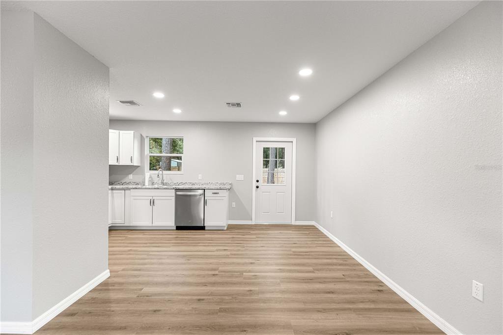 A kitchen with white cabinets and stainless steel appliances opens into a light-floored dining area — 11060 NE 145TH LANE, FORT MC COY, FL