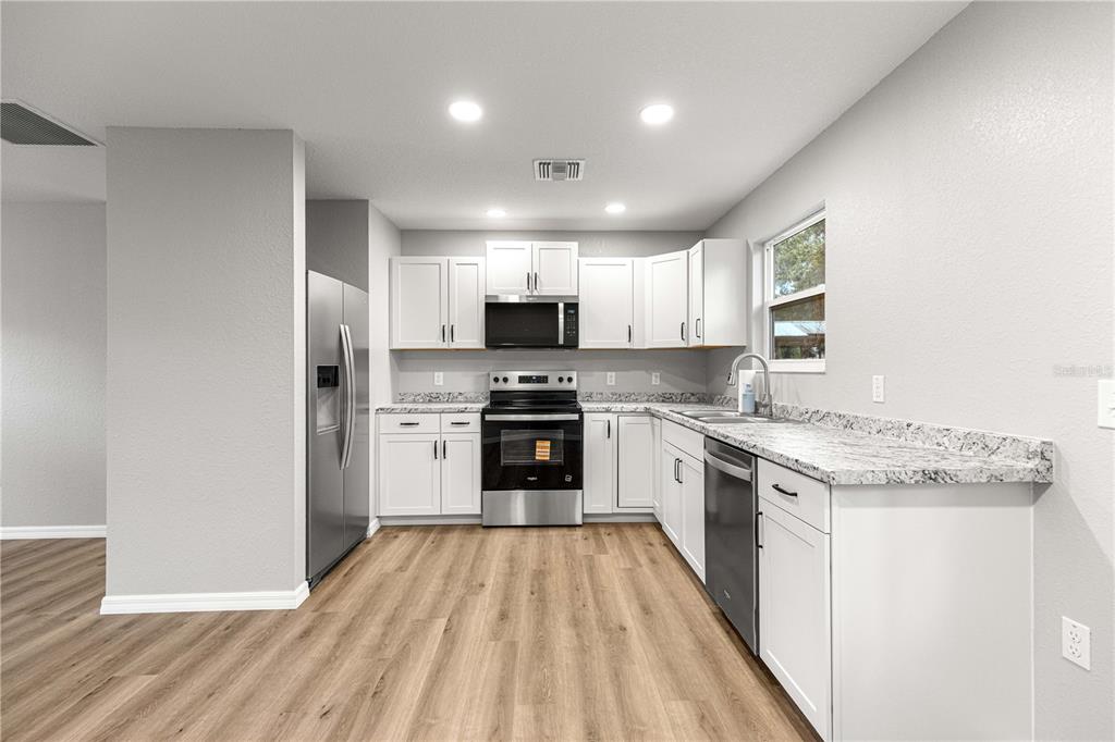 A modern kitchen features white cabinets, granite countertops, stainless steel appliances, and wood-look flooring — 11060 NE 145TH LANE, FORT MC COY, FL