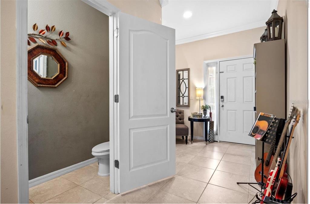 A view from a tiled hallway into a powder room and an entryway with guitars — 3901 SILVERLAKE WAY, WESLEY CHAPEL, FL