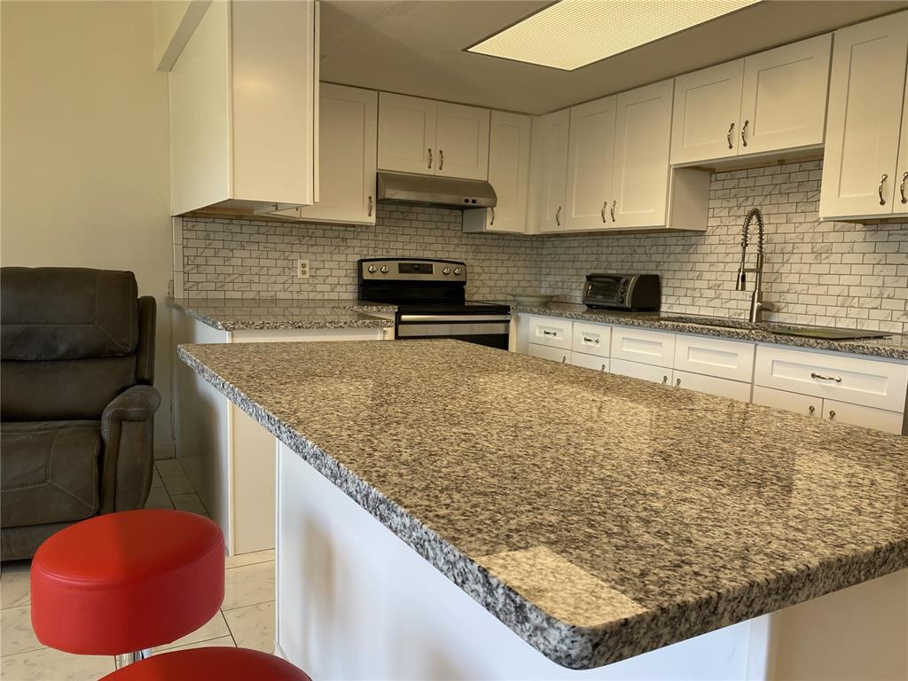 A kitchen features white cabinets, granite countertops, a subway tile backsplash, and a large island — 711 SPRINGER DRIVE UNIT 9, LAKE WALES, FL