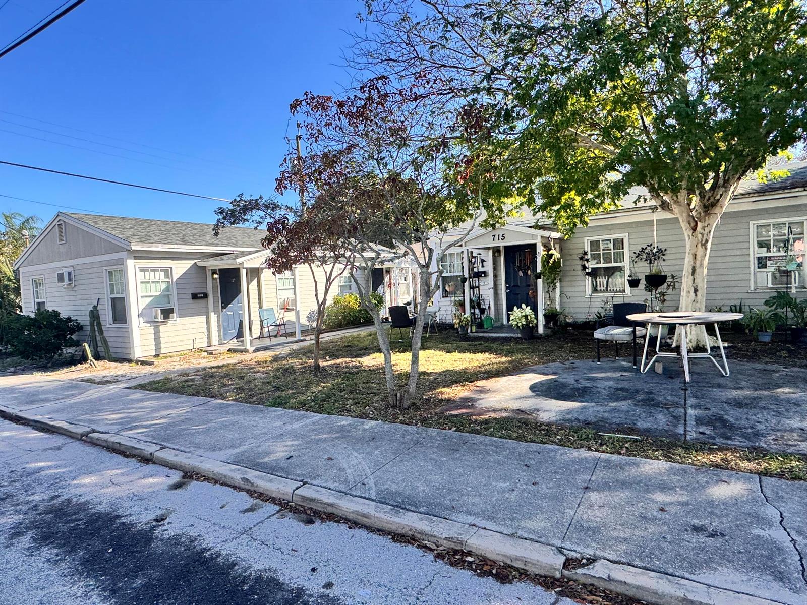 A street-level view of two light-gray single-story houses with a shared front yard and trees — 717 8th Avenue N, FL 33460, FL