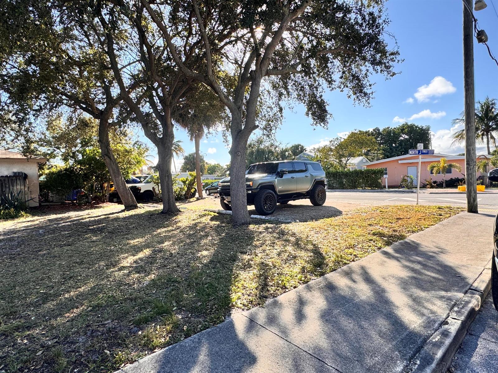 A gray Hummer EV SUV is parked on a grassy lot near a street sign — 717 8th Avenue N, FL 33460, FL