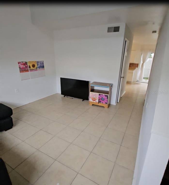 A living room with light tile flooring, a television, and a small storage cabinet — 4008 DOLOMITE STREET UNIT GE, ORLANDO, FL