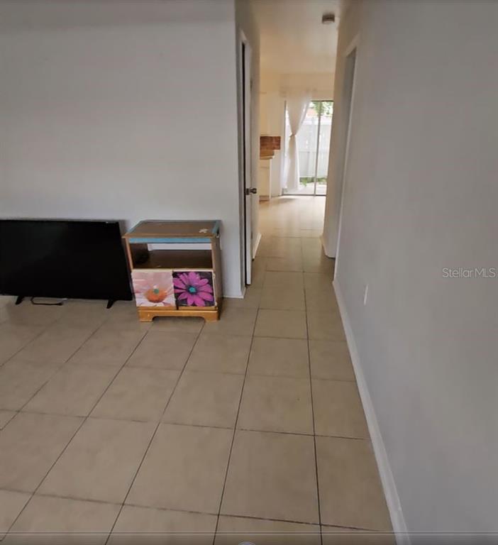A tiled living area features a television on a stand and a hallway leading outside — 4008 DOLOMITE STREET UNIT GE, ORLANDO, FL