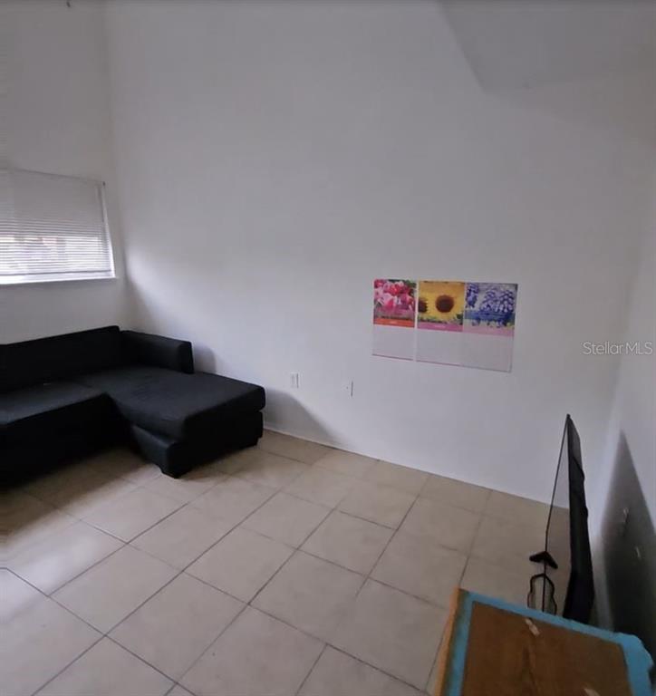 A living room features a black sectional sofa, tiled floors, and wall-mounted floral art — 4008 DOLOMITE STREET UNIT GE, ORLANDO, FL