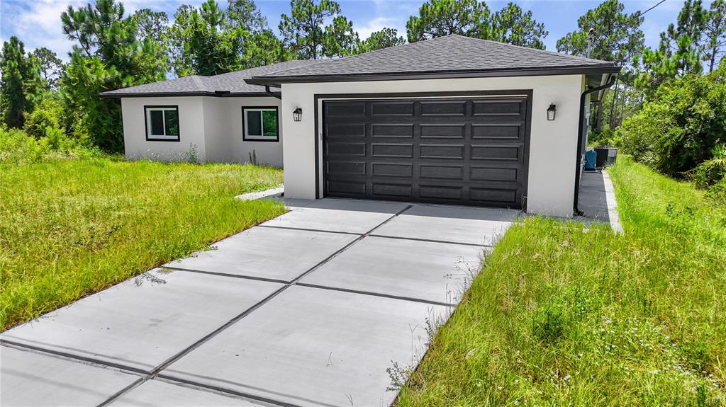 A single-story house with a white exterior, dark garage door, and a concrete driveway — 1142 DUTCHESS STREET E, LEHIGH ACRES, FL