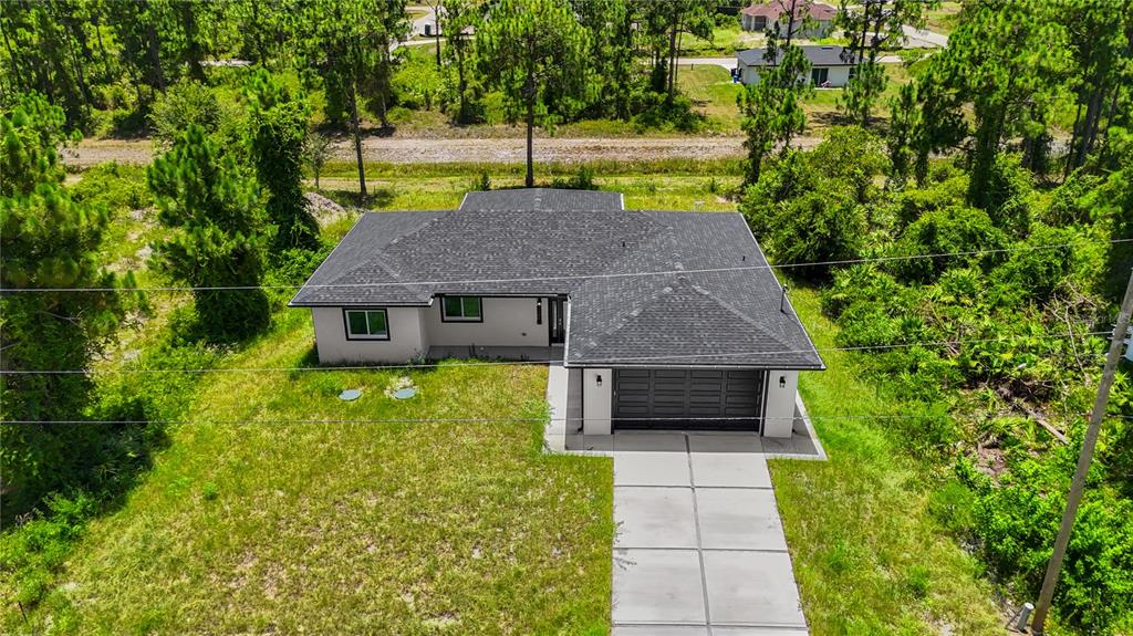 An aerial view shows a single-story house with a dark roof and a concrete driveway — 1142 DUTCHESS STREET E, LEHIGH ACRES, FL