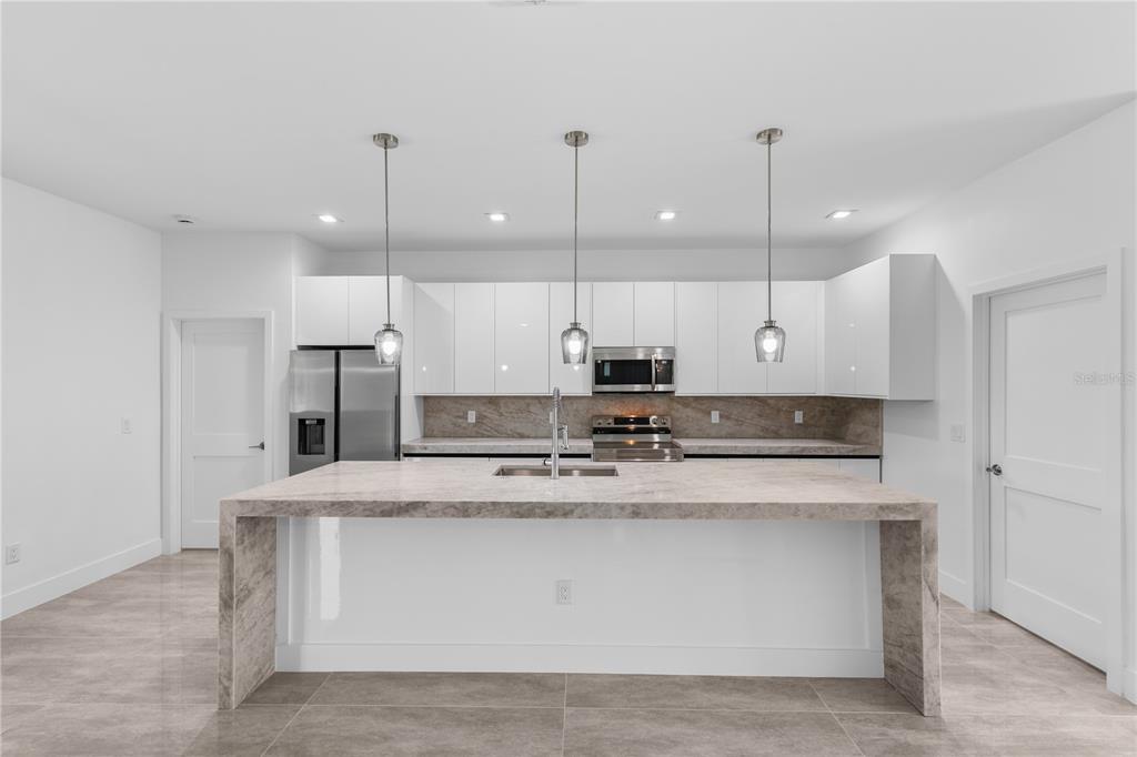 A modern kitchen features white glossy cabinets, a large stone waterfall island, and stainless appliances — 1142 DUTCHESS STREET E, LEHIGH ACRES, FL