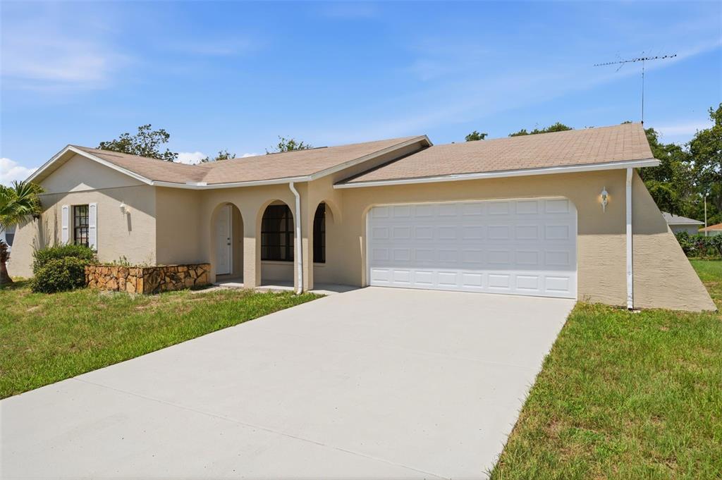 A single-story house with a beige stucco exterior, a two-car garage, and a concrete driveway — 18813 GREEN PARK ROAD, HUDSON, FL