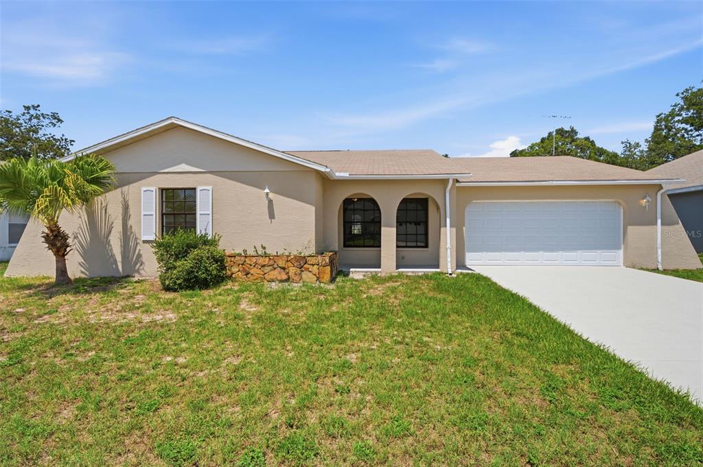 A single-story house with a tan stucco exterior, stone planter, and a two-car garage — 18813 GREEN PARK ROAD, HUDSON, FL