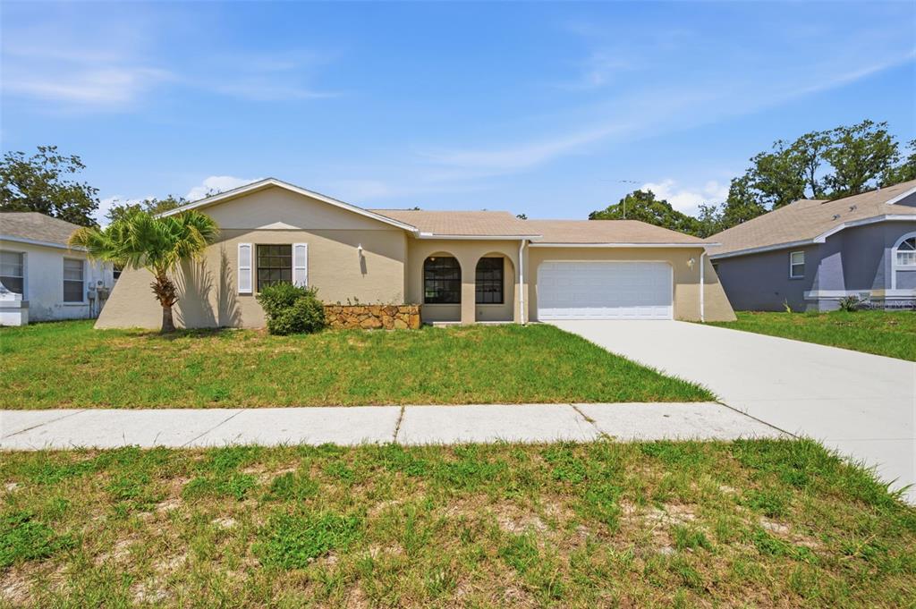 A single-story house with a tan exterior, a two-car garage, and a front lawn — 18813 GREEN PARK ROAD, HUDSON, FL