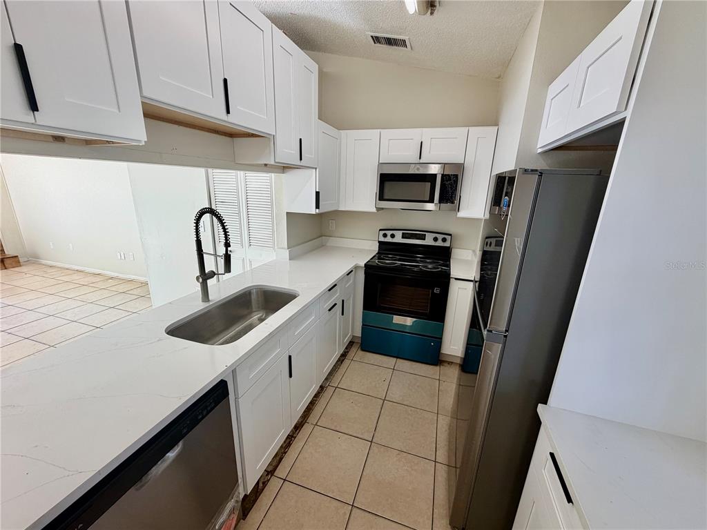A kitchen features white cabinets, stainless steel appliances, a quartz countertop, and tile flooring — 918 OTTO VILLA PLACE UNIT 9, TAMPA, FL
