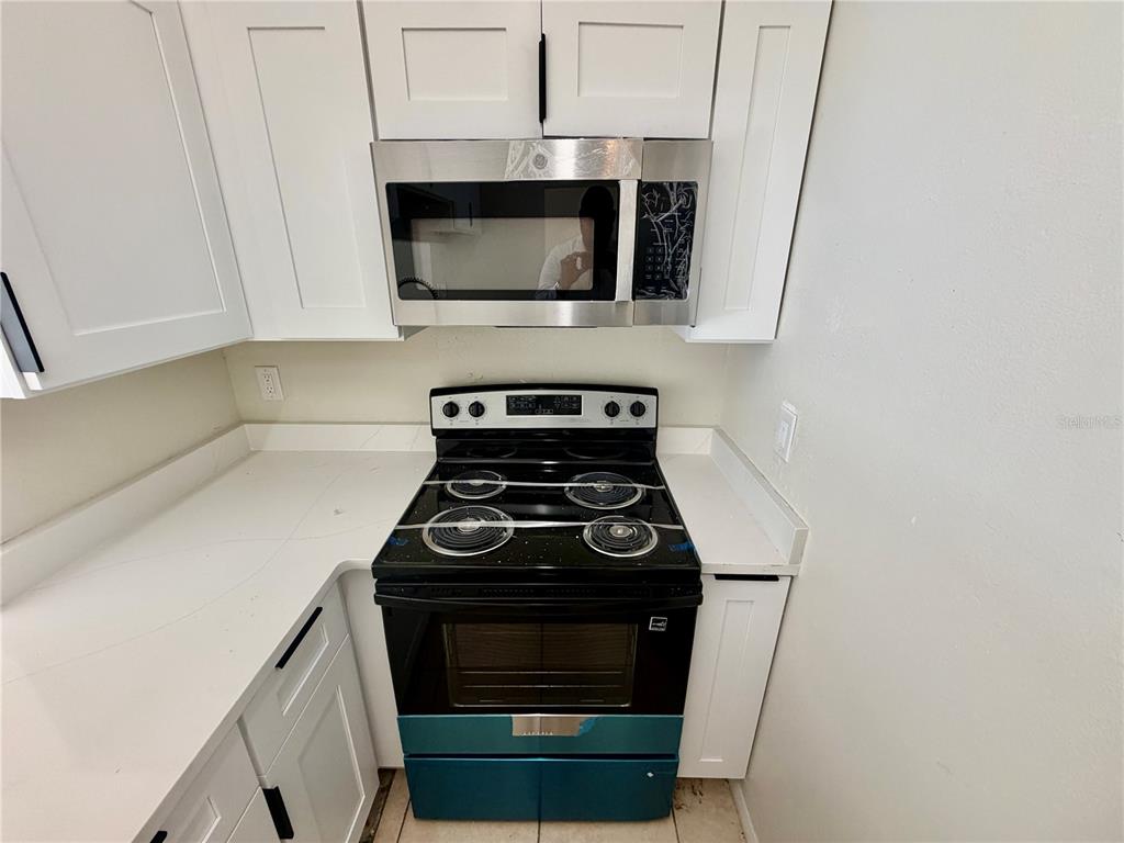 A kitchen features white cabinets, a stainless steel microwave, and a black electric range — 918 OTTO VILLA PLACE UNIT 9, TAMPA, FL