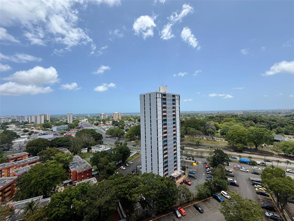 An aerial view shows a tall apartment building surrounded by trees, parking lots, and roads — 1 CLL ALMONTE UNIT 1707, SAN JUAN, PR