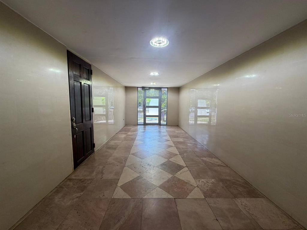 A hallway with tiled floors and beige walls leads to a glass-paneled exterior door — 1 CLL ALMONTE UNIT 1707, SAN JUAN, PR