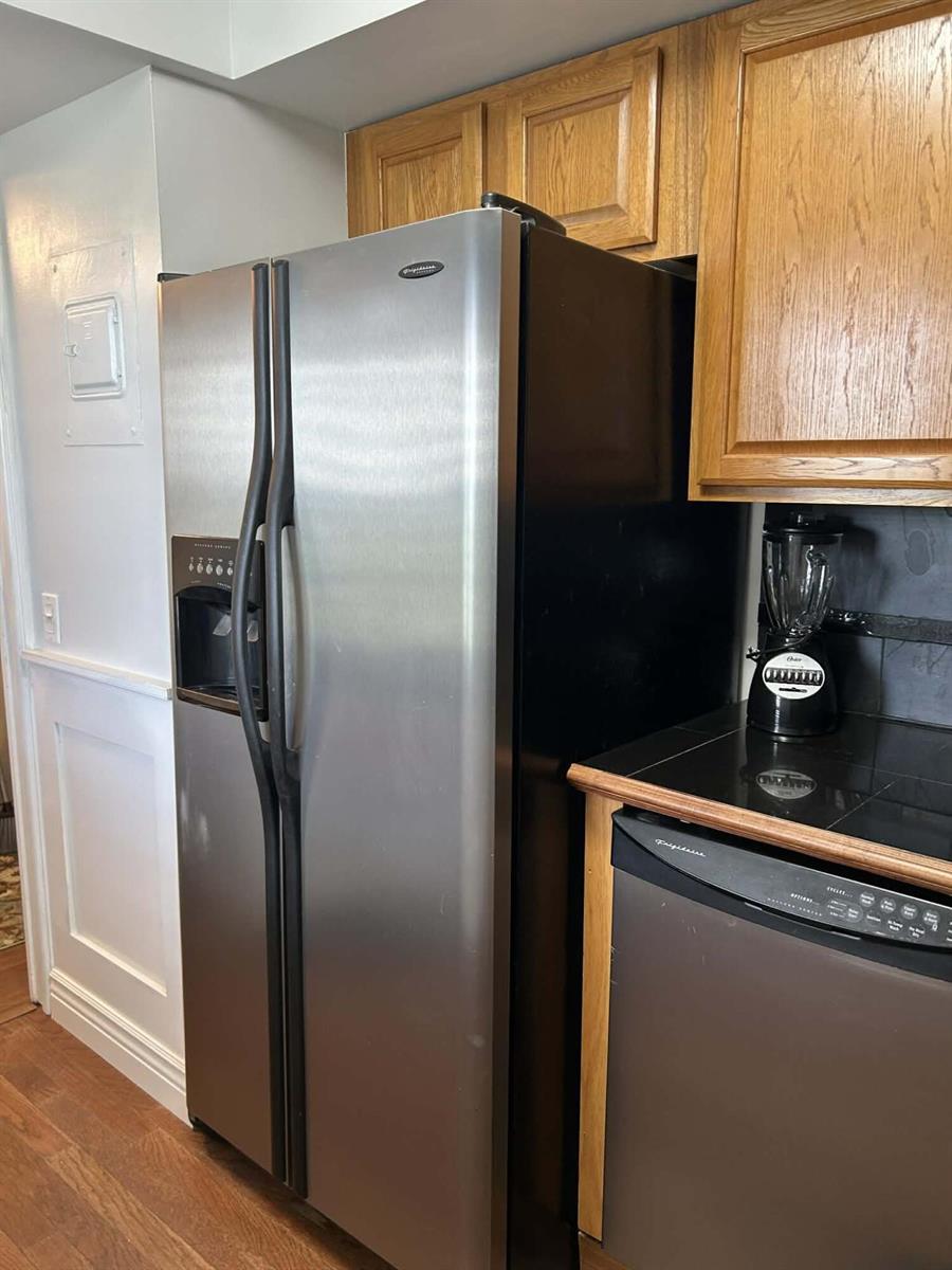 A stainless steel refrigerator stands next to a dishwasher and wooden cabinets in a kitchen — 2651 S Course Drive # 509, Pompano Beach FL 33069, POMPANO BEACH, FL