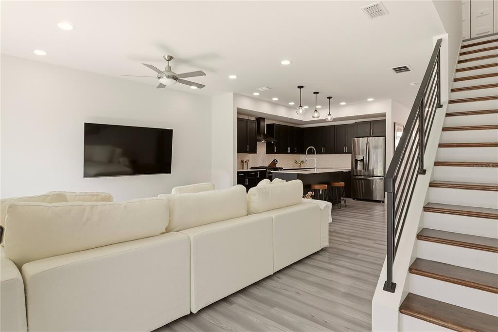 An open-concept living room with a white sectional sofa, wall-mounted television, and adjacent modern kitchen — 3324 SW 49TH TERRACE, GAINESVILLE, FL