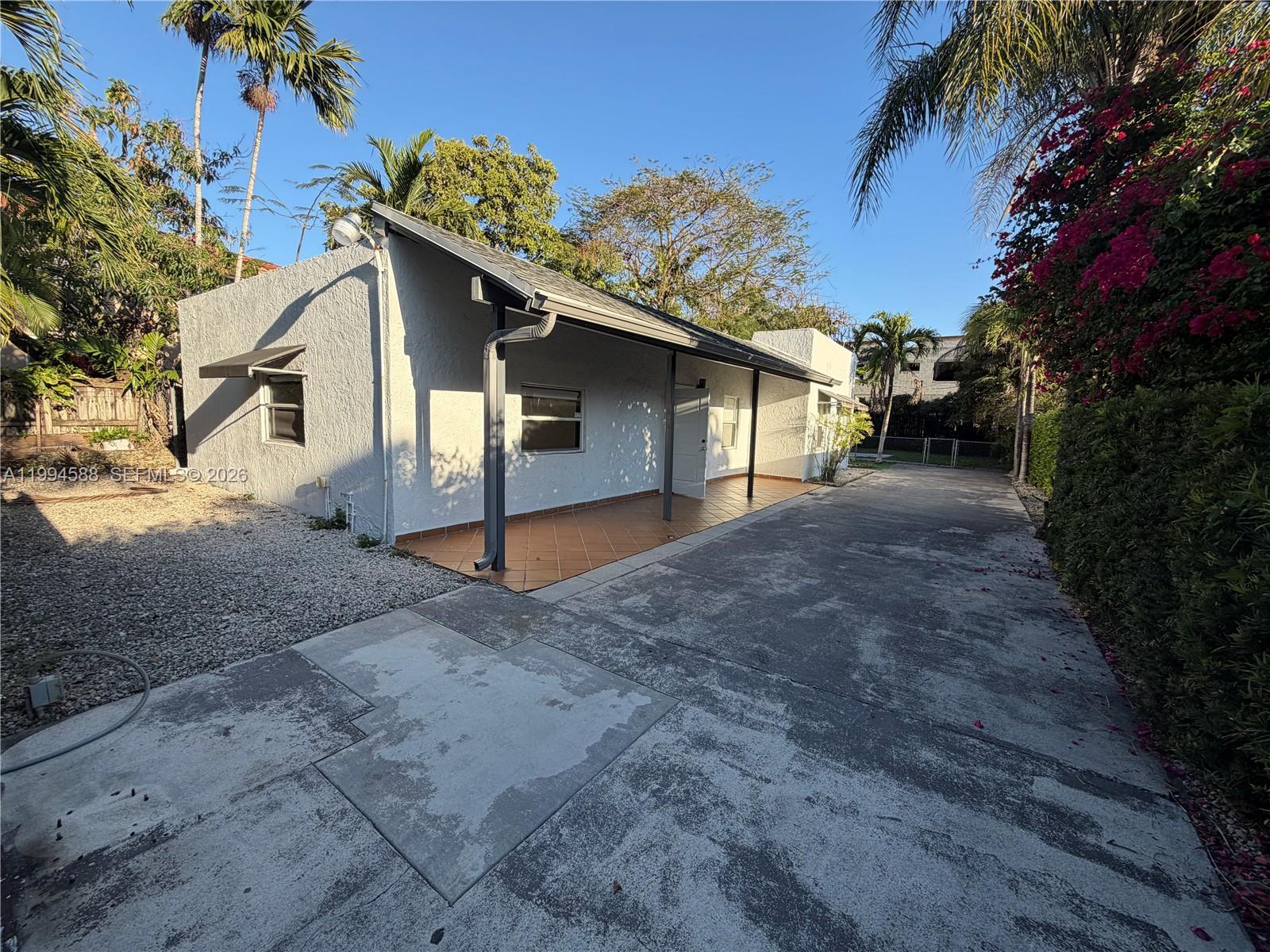 A single-story white house features a tiled porch, a concrete driveway, and surrounding tropical landscaping — 3373 SW 29th Ter, Miami FL 33133, MIAMI, FL