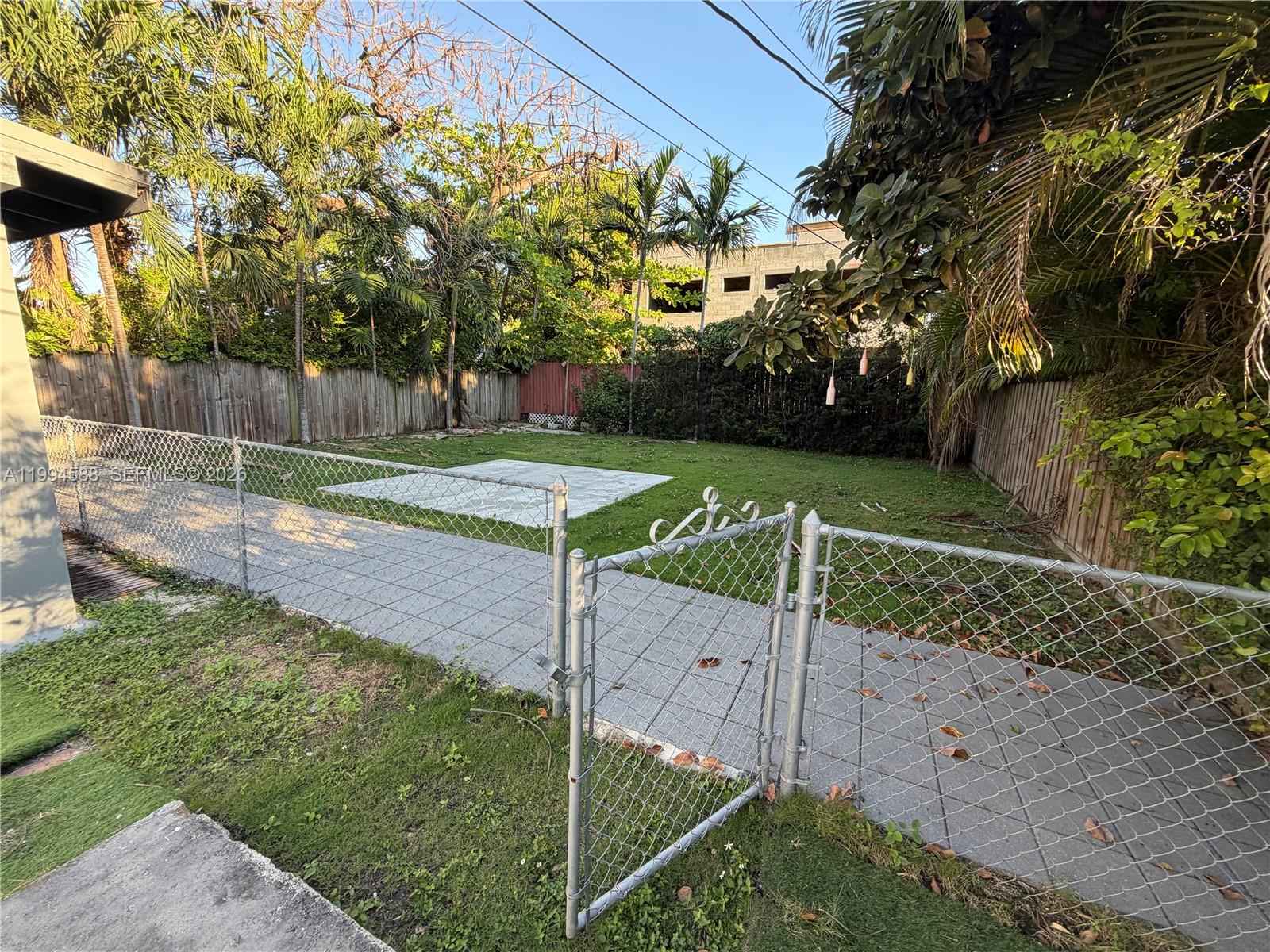 A fenced backyard features a paved walkway, a concrete patio area, and surrounding trees — 3373 SW 29th Ter, Miami FL 33133, MIAMI, FL