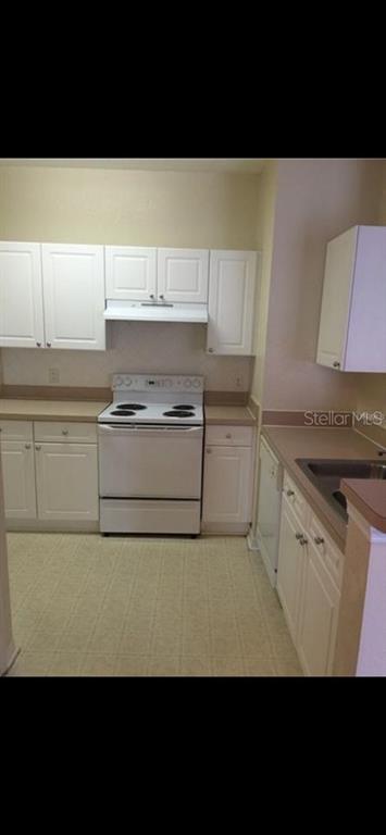 A kitchen features white cabinets, a white electric stove, and tan countertops — 18001 RICHMOND PLACE DRIVE UNIT 220, TAMPA, FL