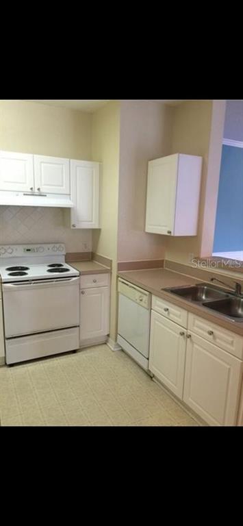 A kitchen features white cabinets, white appliances, and tan countertops — 18001 RICHMOND PLACE DRIVE UNIT 220, TAMPA, FL
