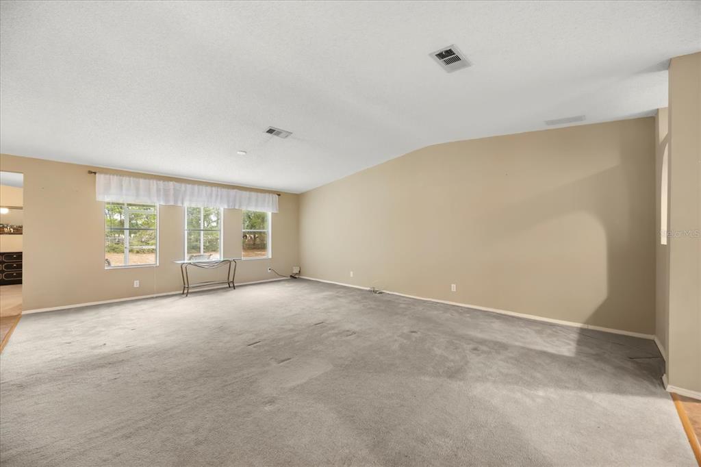 A spacious, empty living room features beige walls, gray carpeting, and three large windows — 2632 LAKE GRASSMERE CIRCLE UNIT 1854, ZELLWOOD, FL