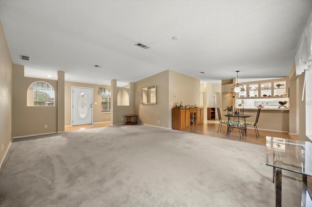 A spacious living room with beige carpet leads to an open dining area and kitchen — 2632 LAKE GRASSMERE CIRCLE UNIT 1854, ZELLWOOD, FL