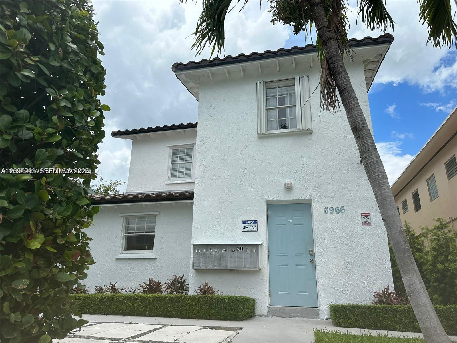 A two-story white stucco building features a light blue front door and exterior mailboxes — 6966 Byron Ave # 101, Miami Beach FL 33141, MIAMI BEACH, FL