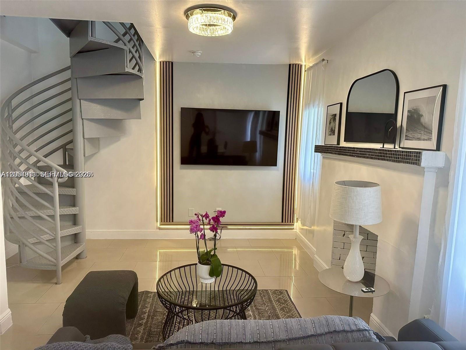 A living room features a spiral staircase, a wall-mounted television, and a fireplace with decor — 6966 Byron Ave # 101, Miami Beach FL 33141, MIAMI BEACH, FL