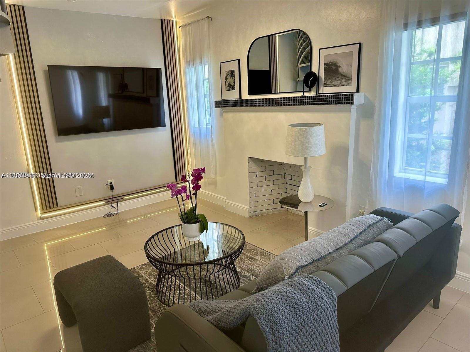 A living room features a wall-mounted television, a fireplace with a mirror, and gray furniture — 6966 Byron Ave # 101, Miami Beach FL 33141, MIAMI BEACH, FL