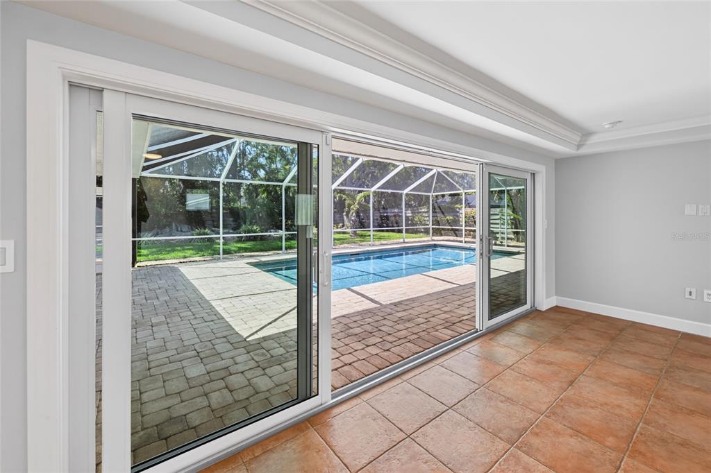 A room with tile flooring features large sliding glass doors opening to a screened-in pool area — 606 OWL WAY, SARASOTA, FL