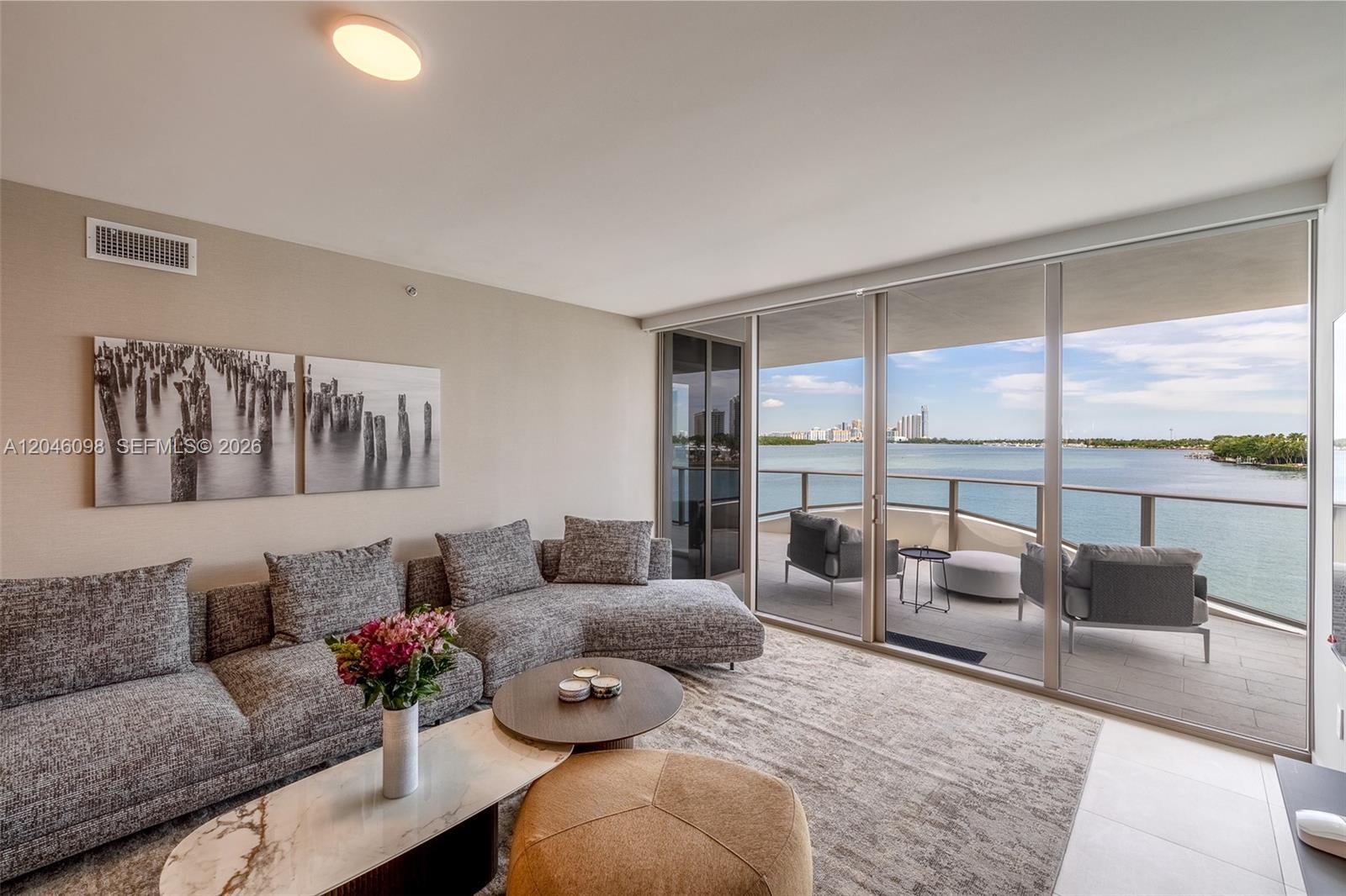 A living room features a gray sectional sofa, coffee tables, and a balcony overlooking water — 1135 103rd St # 405, Bay Harbor Islands FL 33154, BAY HARBOR ISLANDS, FL