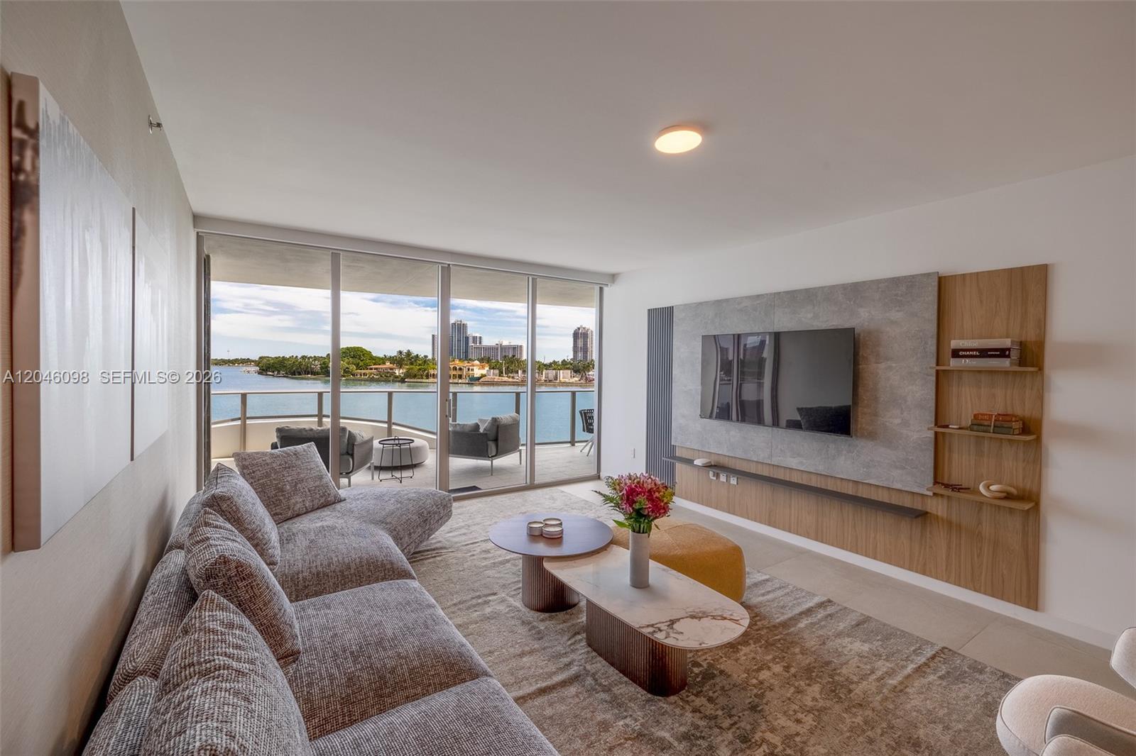 A modern living room features a gray sectional, nested coffee tables, and a balcony overlooking water — 1135 103rd St # 405, Bay Harbor Islands FL 33154, BAY HARBOR ISLANDS, FL