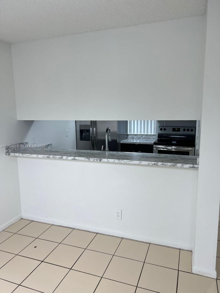 A kitchen pass-through window features a marble-patterned countertop and overlooks a tiled floor area — 8720 N Sherman Cir # 303, Miramar FL 33025, MIRAMAR, FL
