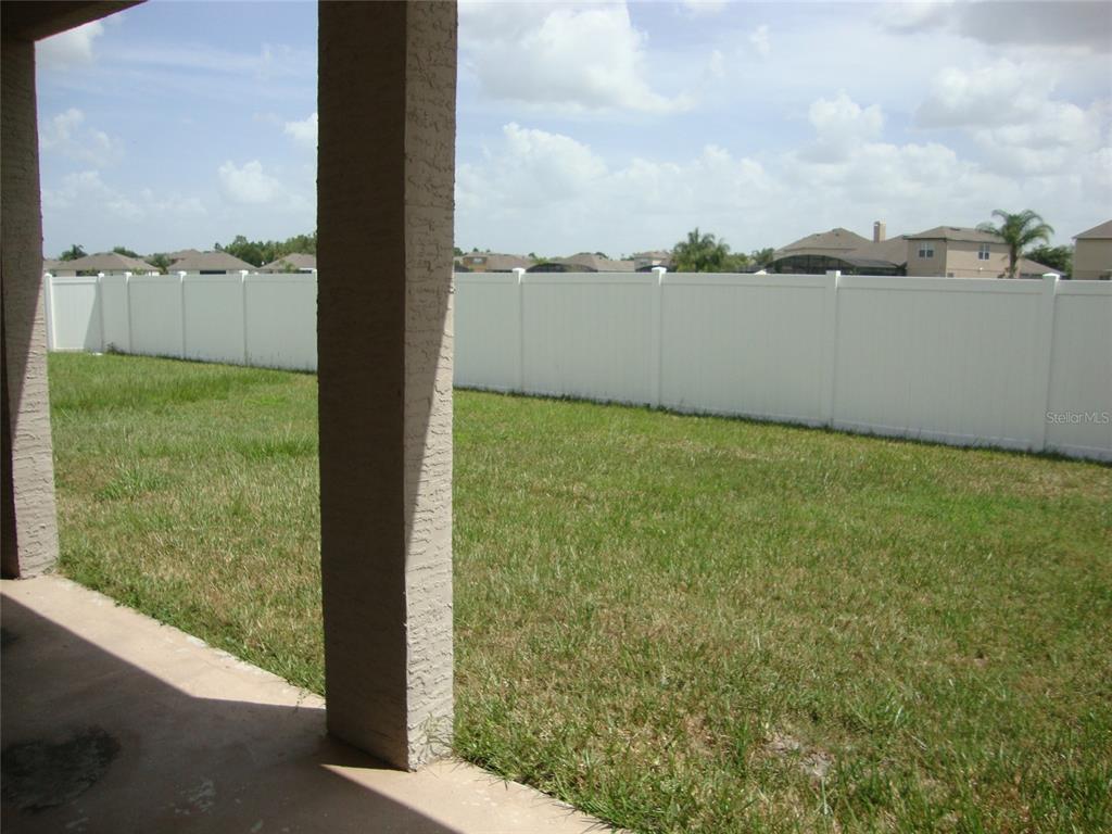 A view of a grassy backyard enclosed by a white vinyl fence from a patio — 4984 BIRCH STONE LANE, ORLANDO, FL