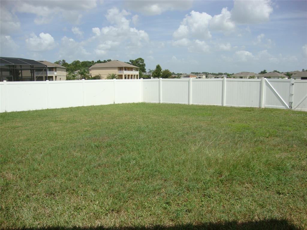 A grassy backyard is enclosed by a white vinyl privacy fence under a cloudy sky — 4984 BIRCH STONE LANE, ORLANDO, FL