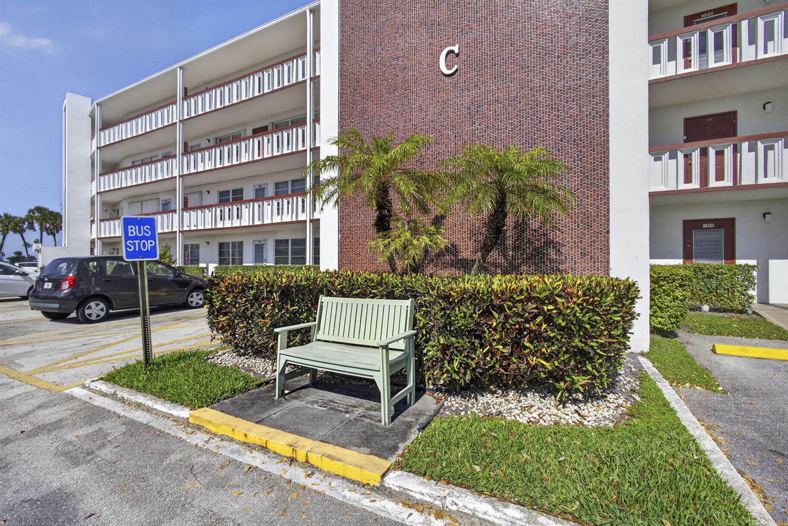 A light green bench sits in front of a brick apartment building marked with a C — 105 Greenbrier C, West Palm Beach FL 33417, WEST PALM BEACH, FL
