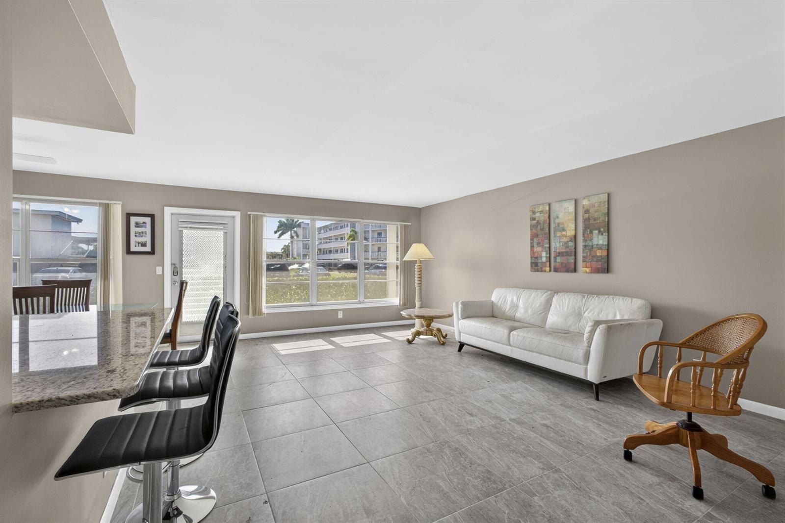 A living room features gray tile flooring, a white sofa, and a kitchen breakfast bar — 105 Greenbrier C, West Palm Beach FL 33417, WEST PALM BEACH, FL